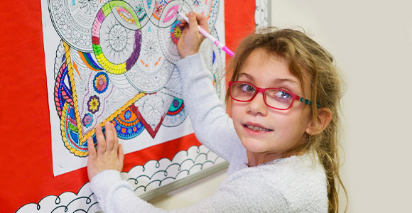 Elementary school special education girl coloring mandala poster on bulletin board.