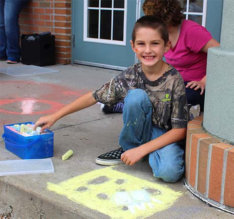 An elementary school boy smiles while drawing with chalk outside his special education school.