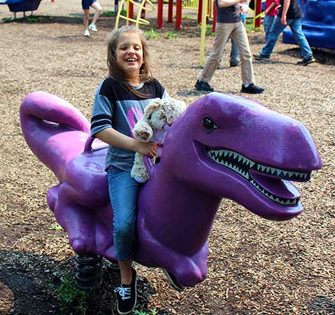 An elementary school students laugh from atop a purple dinoaur riding toy.