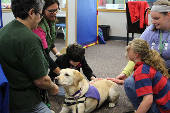 Special needs students pet a dog and smile as their teachers look on