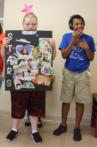 A student in an autism support program shows off his school project while a friend smiles beside him.