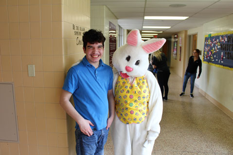 A special education student in a blue shirt poses and smiles with the Easter bunny.