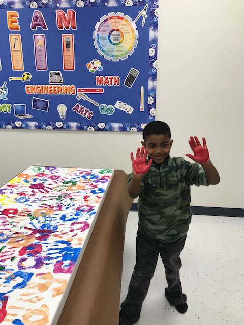 A special education student shows off his paint-covered hand near an art project