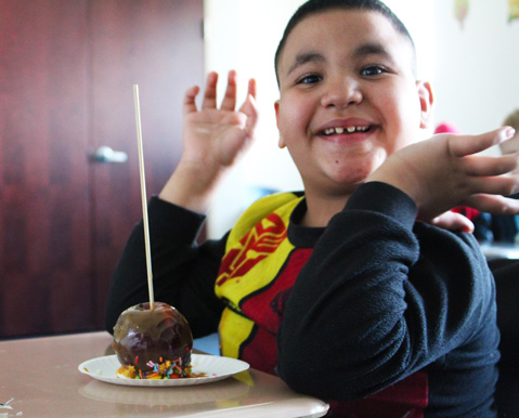 A young boy smiles over his caramel apple at his special education school.