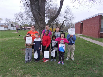 An elementary autism support class shows off bags by a tree outside of their special education school.