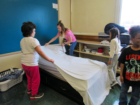 Three students in an autism support program work with their special education teacher on making a bed 