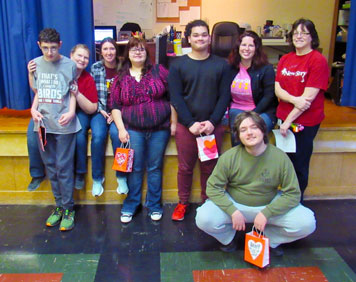A group of special education students and teachers smile while holding Valentine bags. 