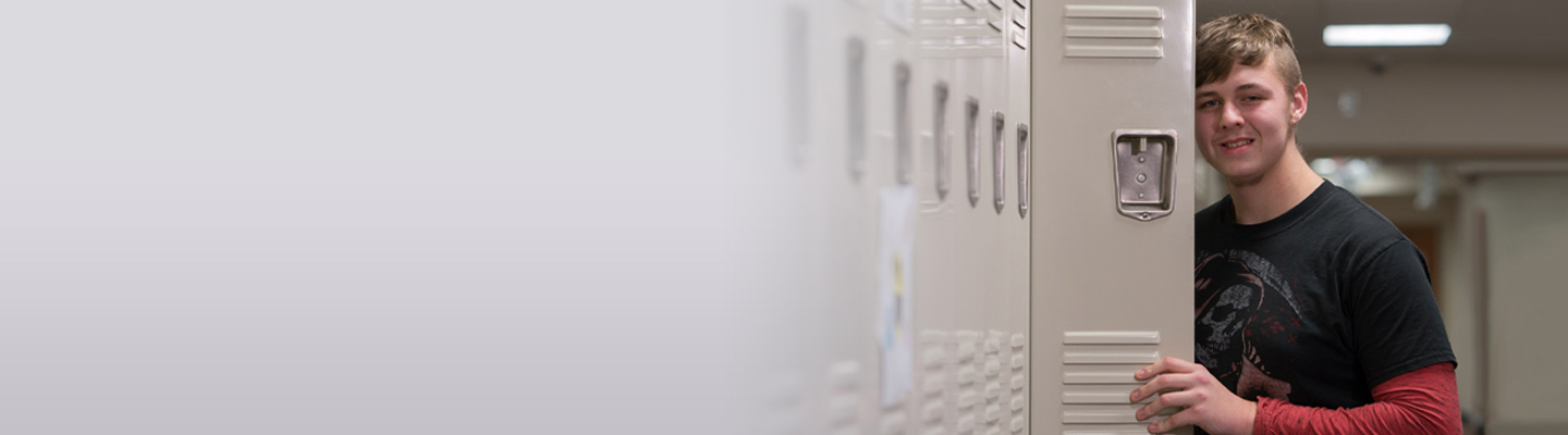 A high school student smiles from behind his locker at a special education school.