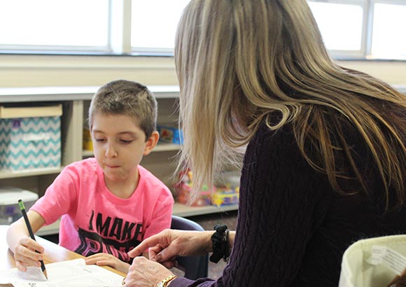 An occupational therapist helps a young boy at his special education school learn to hold a pencil.