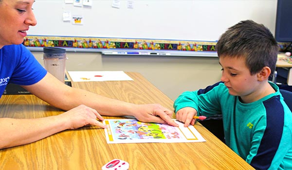 An elementary school student writes as his special education teacher looks on.