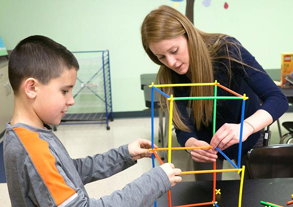 Special Education teacher and elementary student work together at a school to build a structure.