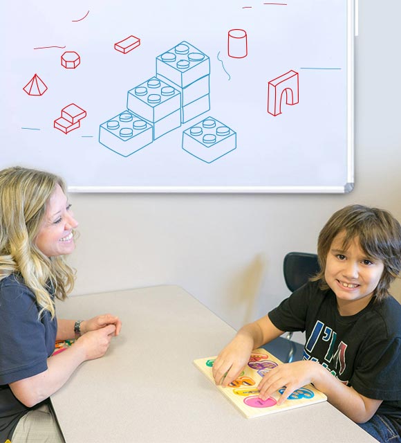 Happy elementary school special education boy completing his numbers lesson with speech therapist.