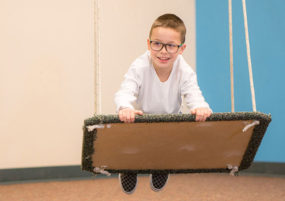 Elementary school special education boy on platform swing during occupational therapy session.