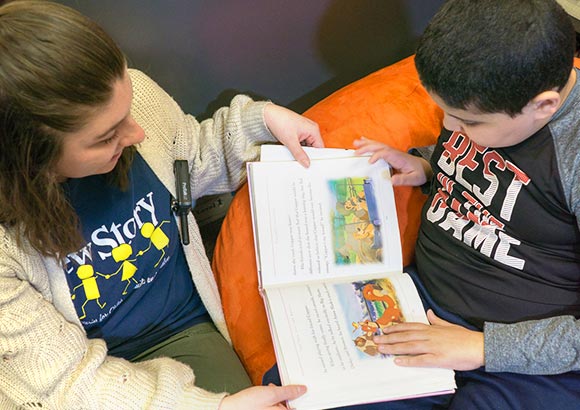 Staff member helping elementary school special education boy with reading, while sitting on a bean bag chair.