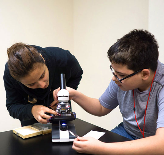 High school boy with special education teacher looks under a microscope as part of his STEAM program