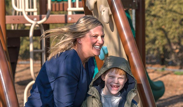 Giggling staff member and elementary special education boy playing outdoors at a jungle gym.