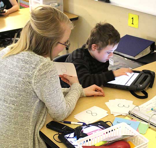 An elementary school boy and his special education teacher use an assistive device as he works on counting.