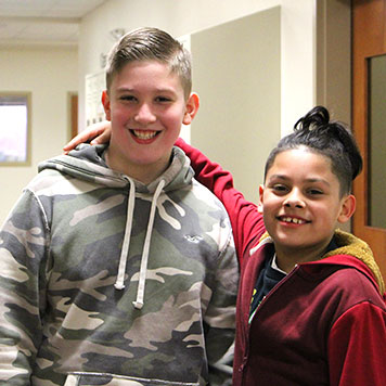 Two middle school boys smile at the camera from the hallway of their special education school.