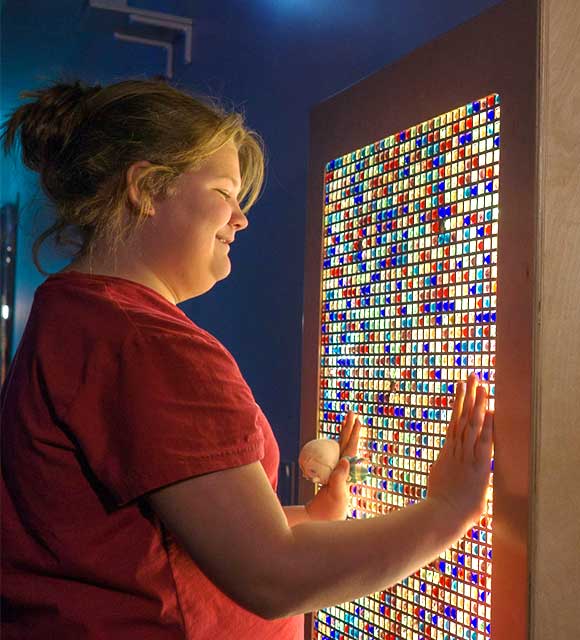 High school girl smiles in front of a multi-colored light box as part of her sensory education program.