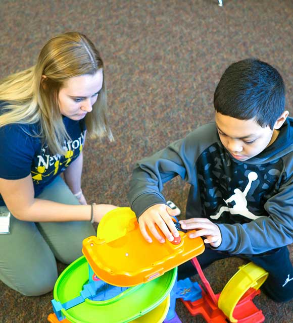 Staff member working with elementary special education boy learn through play using toy car track.