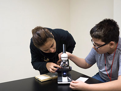 High school boy with special education teacher looks under a microscope as part of his STEAM program.