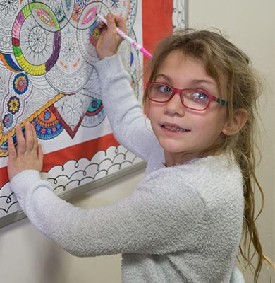 Elementary school special education girl coloring mandala poster on bulletin board.