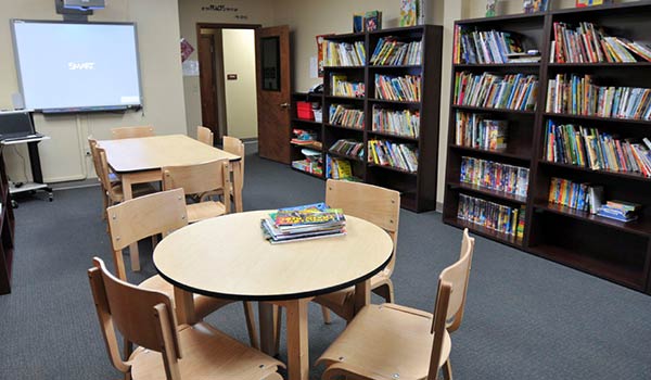 This special education school library is full of books, tables for reading, and features a smart board.