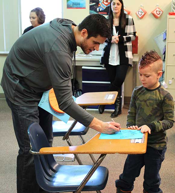 An elementary school student with a mohawk looks on as his special education teacher reviews and assignment.