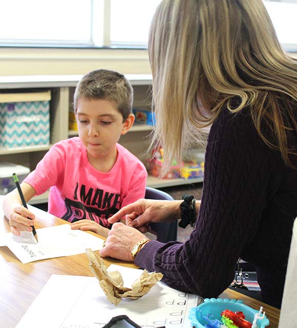 Happy elementary school special education boy completing his numbers lesson with speech therapist.