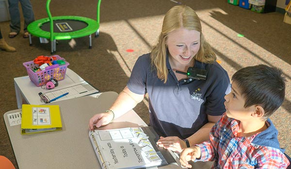 Special education teacher providing education lesson on days of the week to elementary school boy with autism.