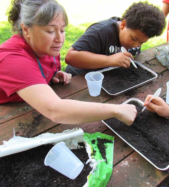 A special education teacher works with several students to plant seeds during an outdoor lesson.
