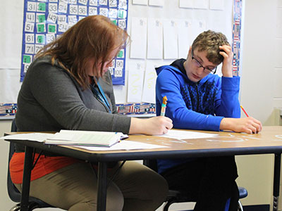 A high school boy and special education teacher work on an activity together.