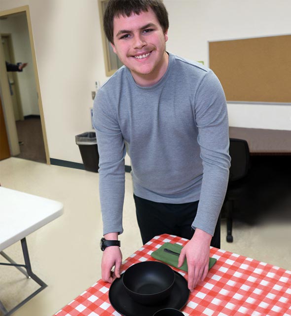 Special education teen boy, in the Transition program, practices setting a table as part of developing life skills.