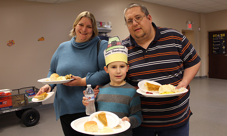 a young male student, his mother and father hold their thanksgiving plates. They are smiling wide!