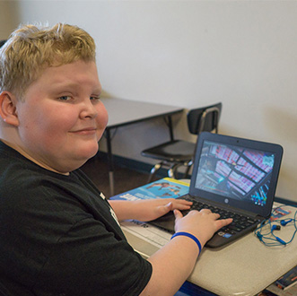 Smiling young boy at school uses computer as part of his educational program