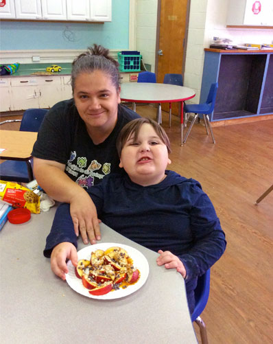 Special education teacher and student smile together over a snack