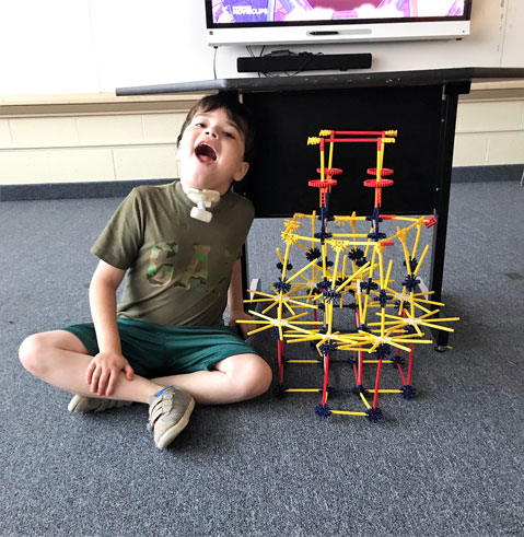 A young boy in his special education classroom smiles while working with building toys