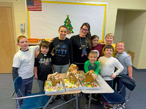 An elementary special education classroom smiles as they pose with gingerbread houses