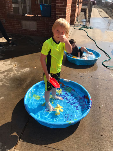 A young boy playing with water during a lesson gives the camera a thumbs up