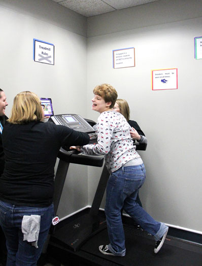 A special needs student runs on a treadmill as her teachers watch