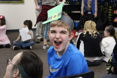 A boy in a blue shirt and leprochaun hate smiles for the camera at his special education school.