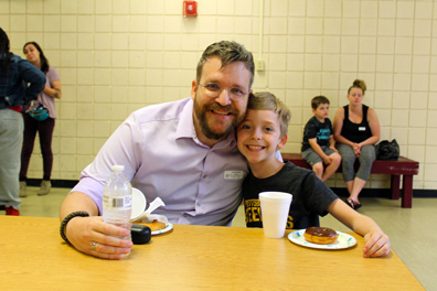 A young boy smiles with his father during an event at his school.