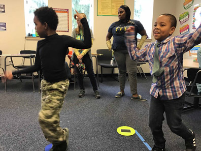 Two young boys dance as their special education teacher watches.