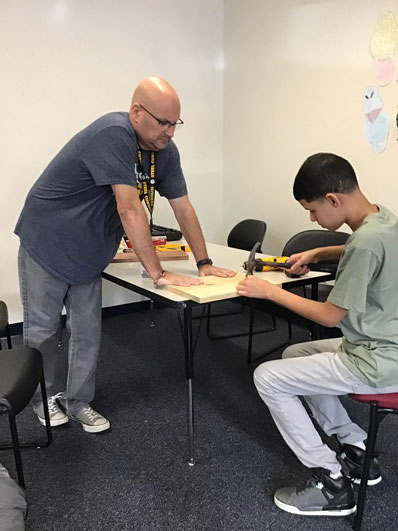 A special education student works with a hammer as his teacher looks on