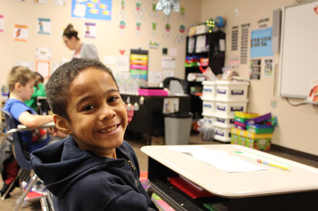 A young boy smiles at the camera from his special education classroom