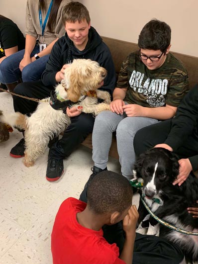 Two special education students pet a white dog during an event at their elementary school.