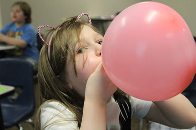 A special education student blows up a pink balloon while wearing cat ears.