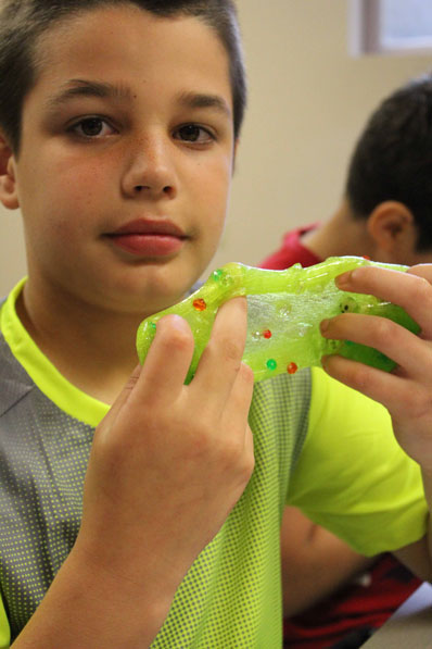 A student with an autism spectrum diagnoses plays with slime and looks at the camera.