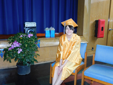 A special education student in a yellow cap and gown awaits a graduation ceremony. 