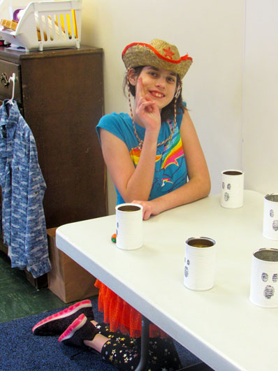 A special education students wearing a straw hat smiles in front of a project she is working on 